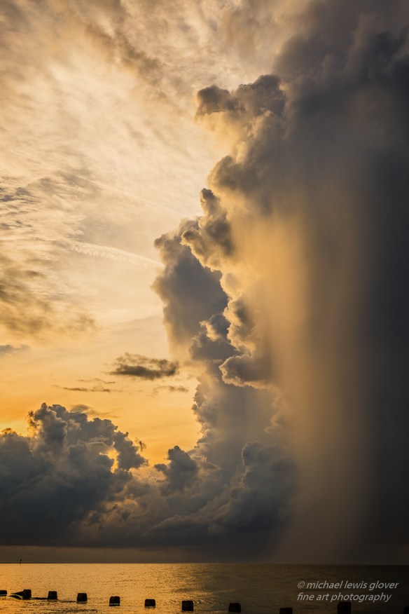Taken on Honeymoon Island in Dunedin, Florida. A massive storm cloud passing through close to sunset drops a beautiful glowing rain shower.